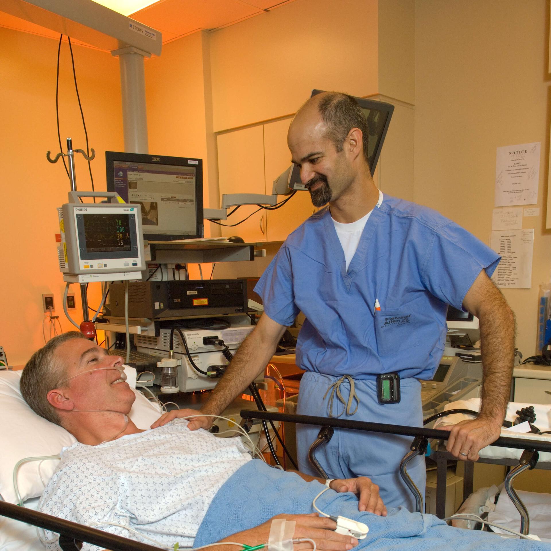 A doctor conversing with a patient who is laying down in a hospital bed.