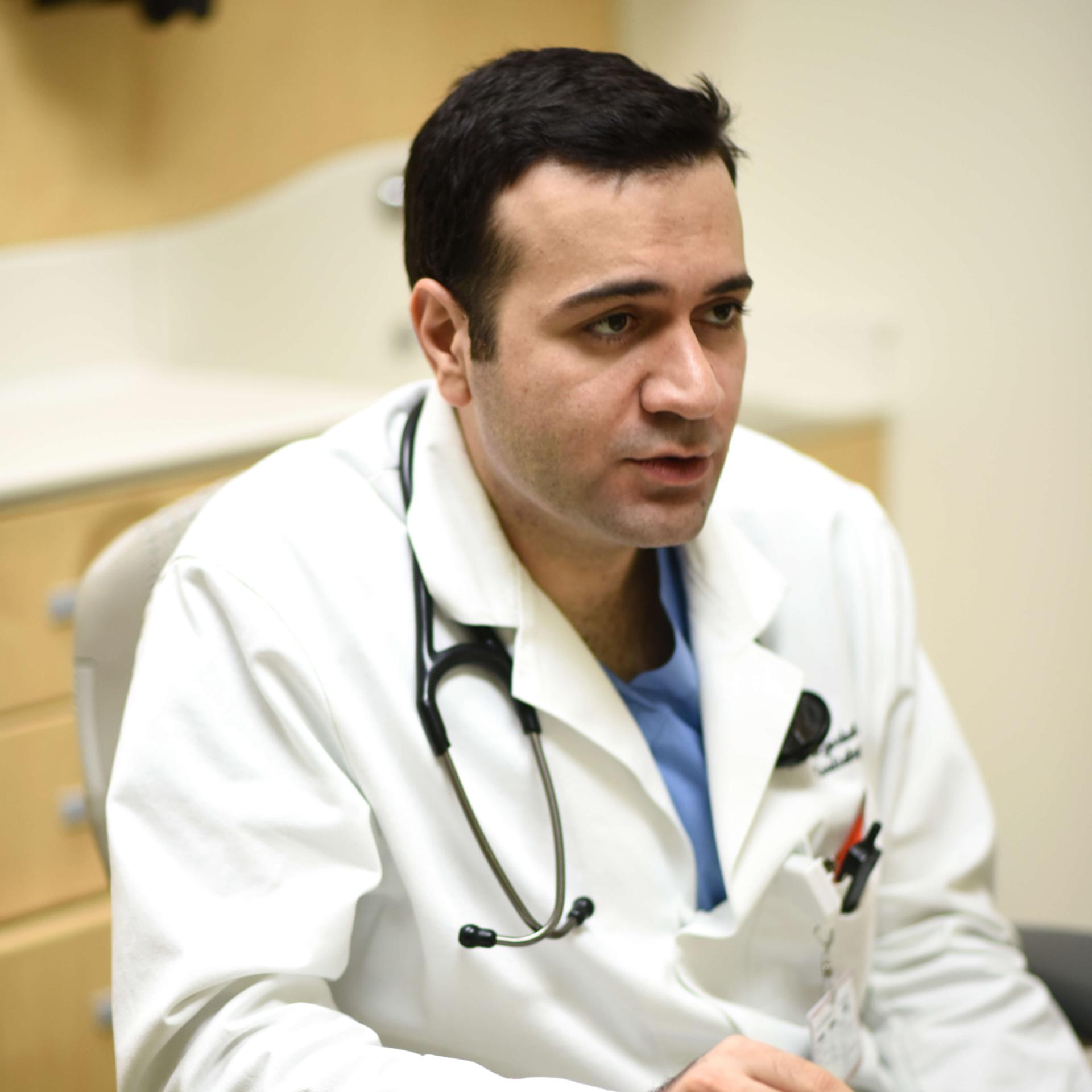 A person sitting wearing a stethoscope and lab coat