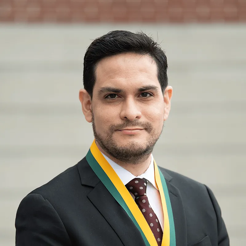 Headshot image of the researcher adorned with an award, posed outdoors in front of a distant building.