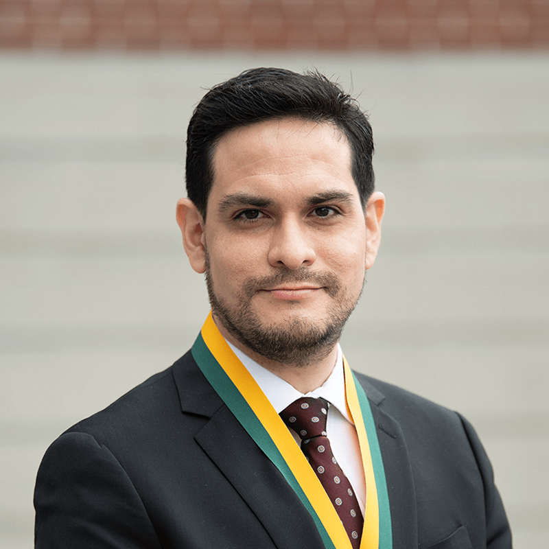 Headshot image of the researcher adorned with an award, posed outdoors in front of a distant building.