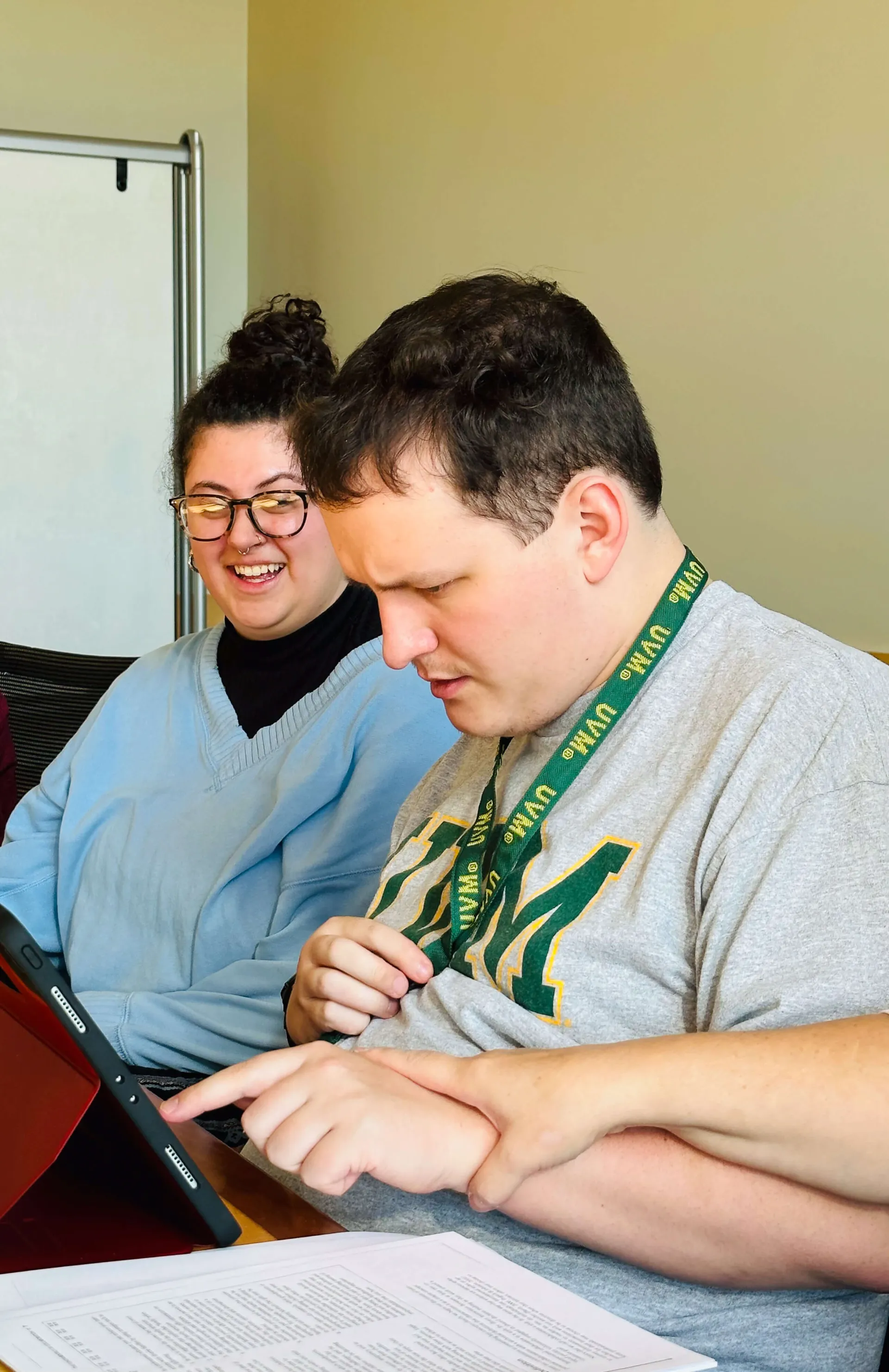 A college student works on an assistive communication device as a communication support person looks on