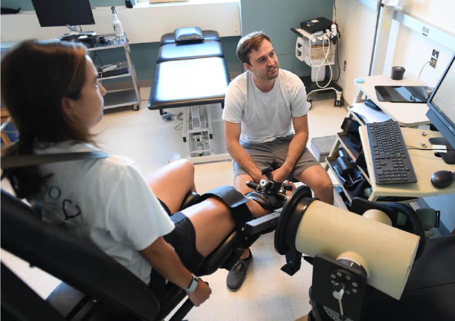 Person with leg in an imaging device while another looks at image display