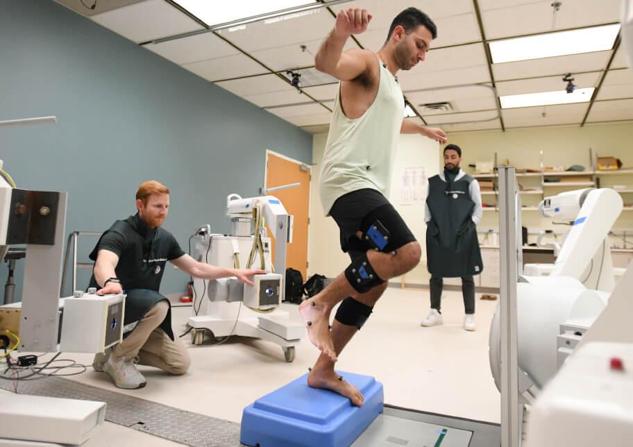 person balancing on one foot while two practitioners observe