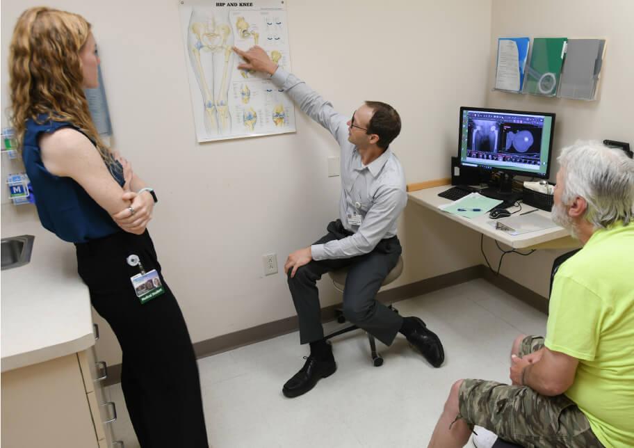 patient and two providers look at anatomical chart on a wall