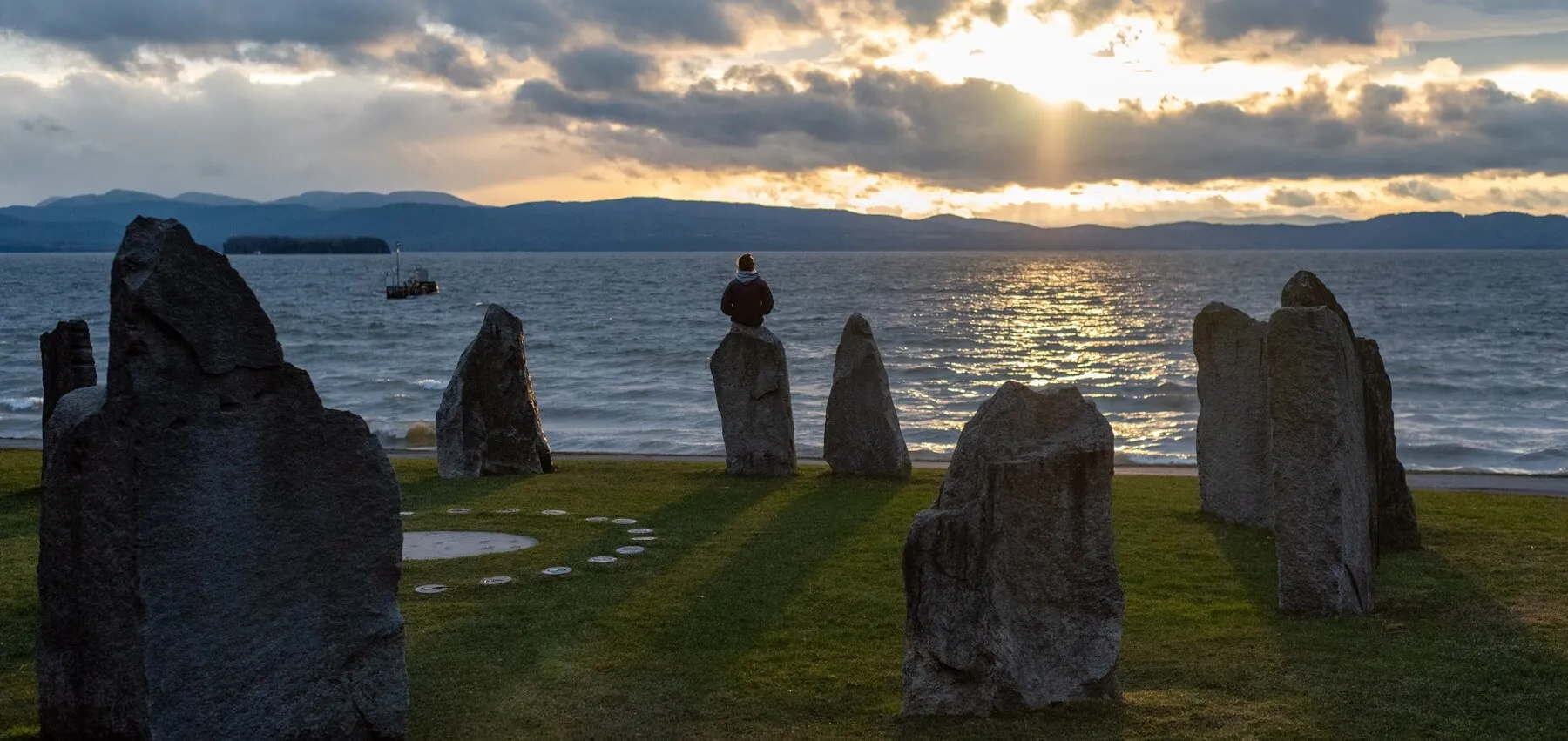 A person sitting on top of a rock positioned in a circle formation next to a lake