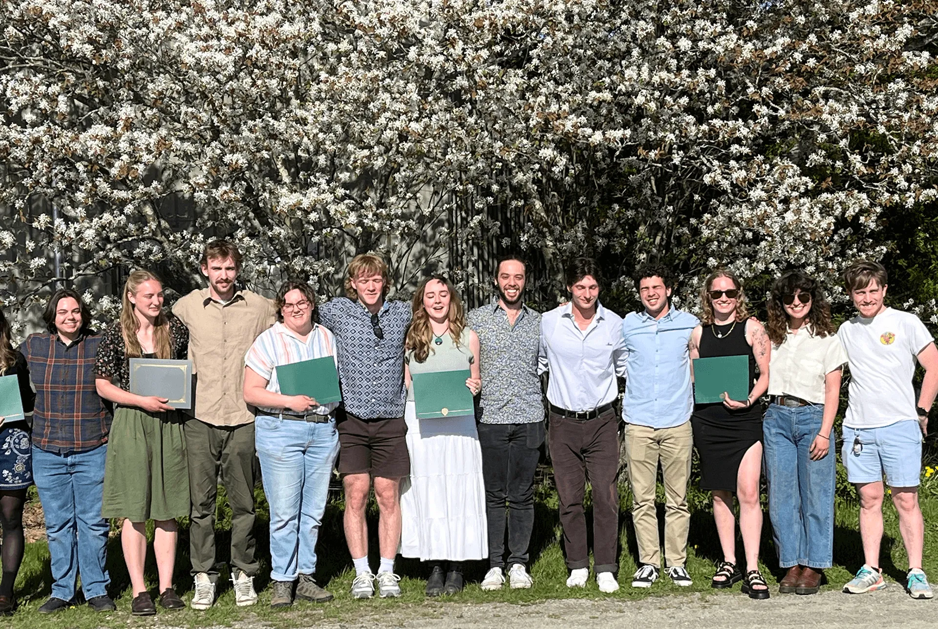 Students with awards standing in a row in front of flowering trees