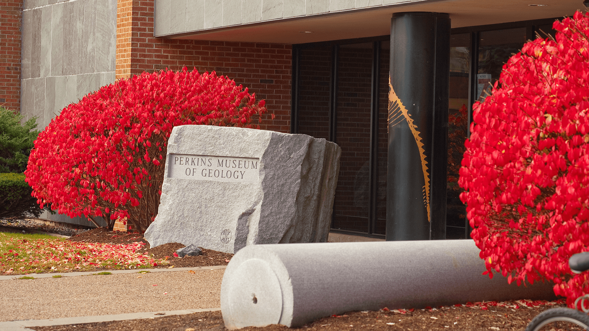 A large rock positioned prominently in front of a building, contrasting natural and architectural elements
