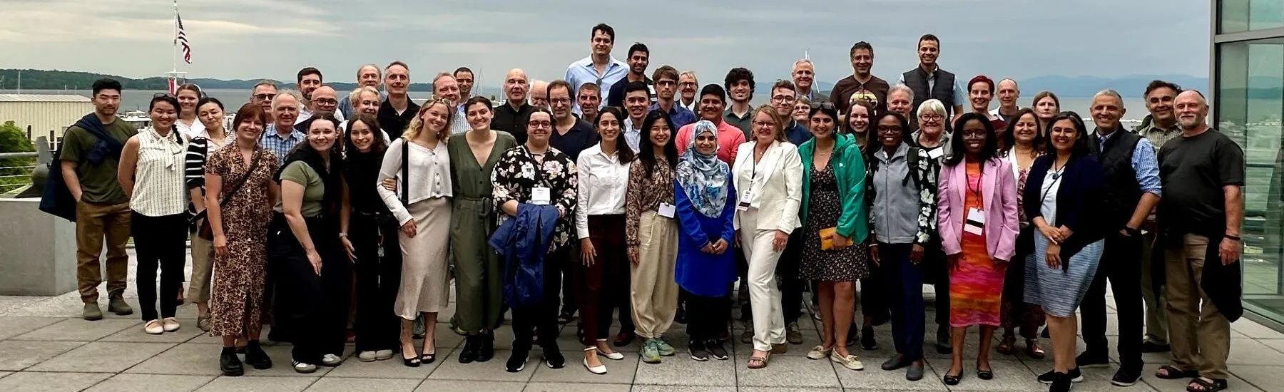 A large group of people happily posing together in front of a body of water.