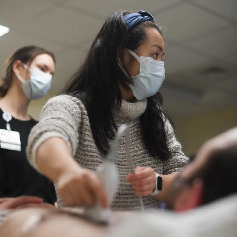 Two medical students practice ultrasounding on a person's abdomen.