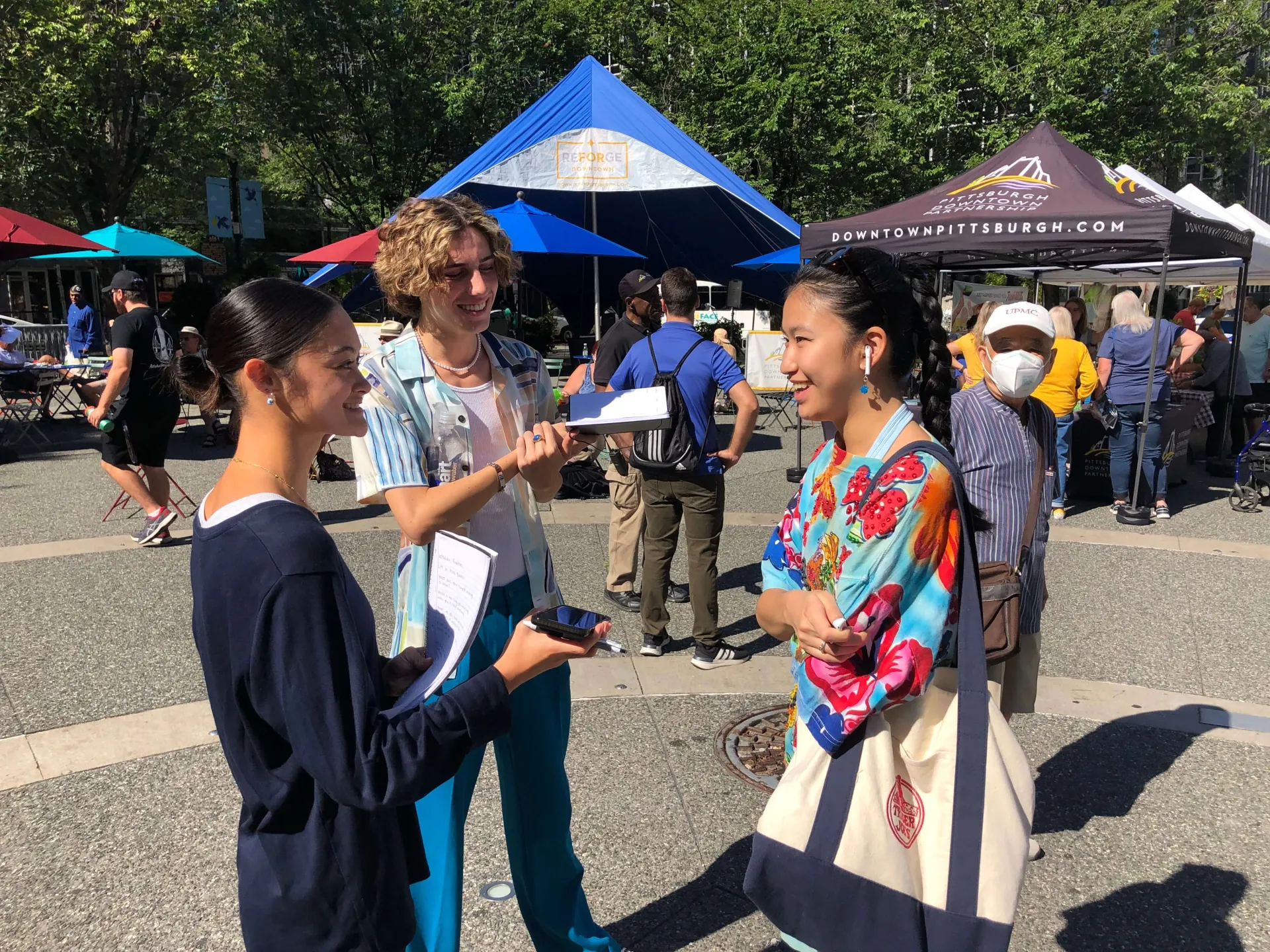 Two student reporters interview a local farmers' market with audio recorders in hand.