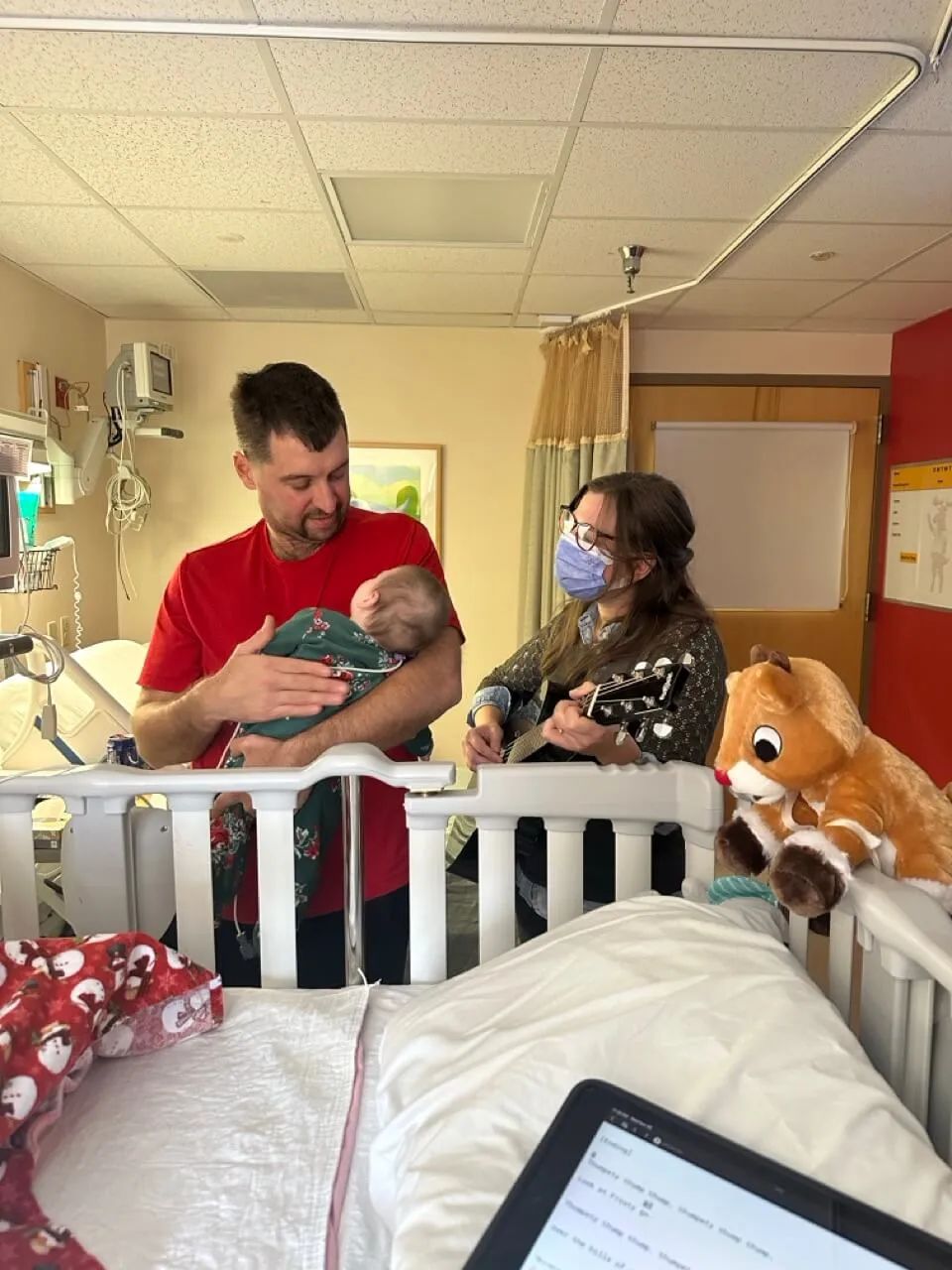Man holding a baby and singing while a music therapist plays guitar