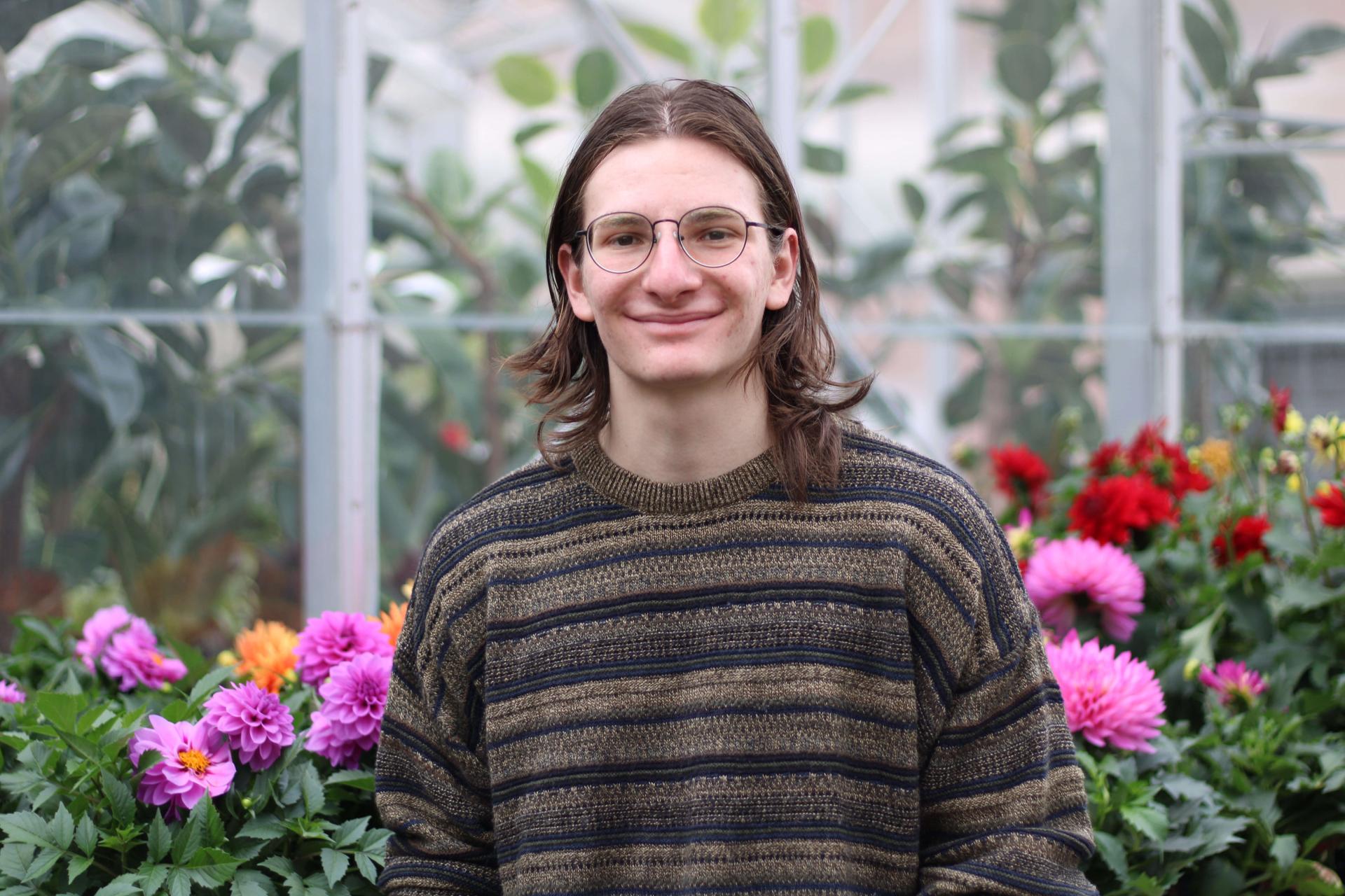 Student in greenhouse looking at camera with flowers in background