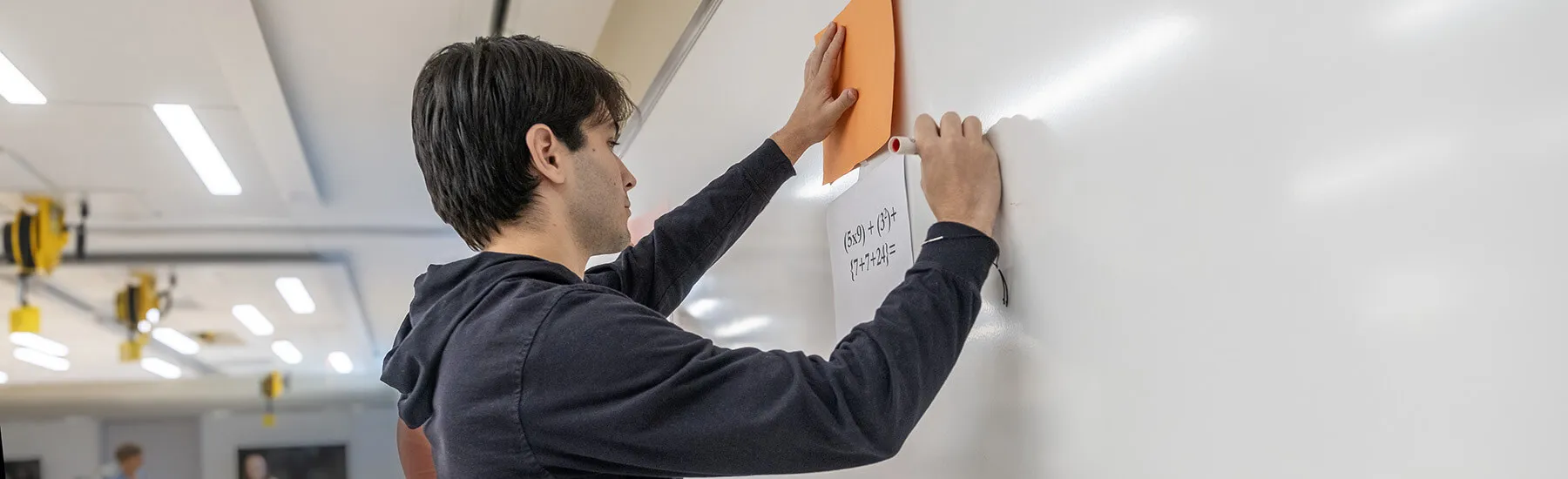 Math student solves an equation on the white board during a competition against faculty