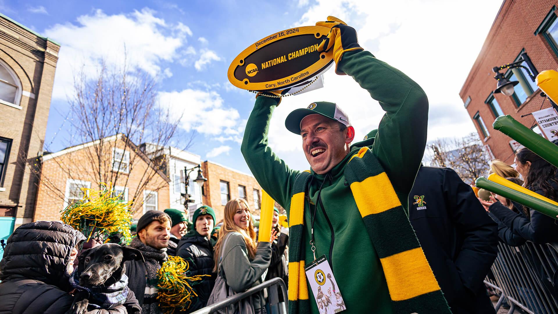 Coach Dow holding up trophy in a crowd of people on Church Street