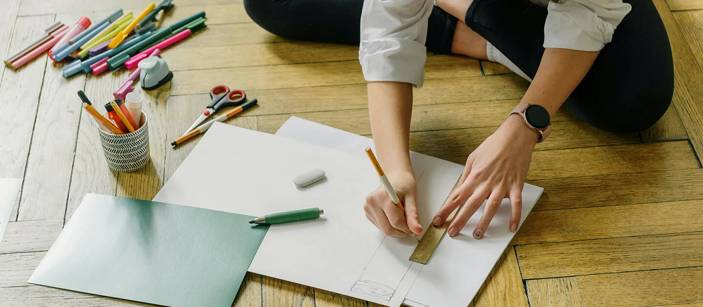 a person cross-legged on the floor sketching something on a large piece of paper