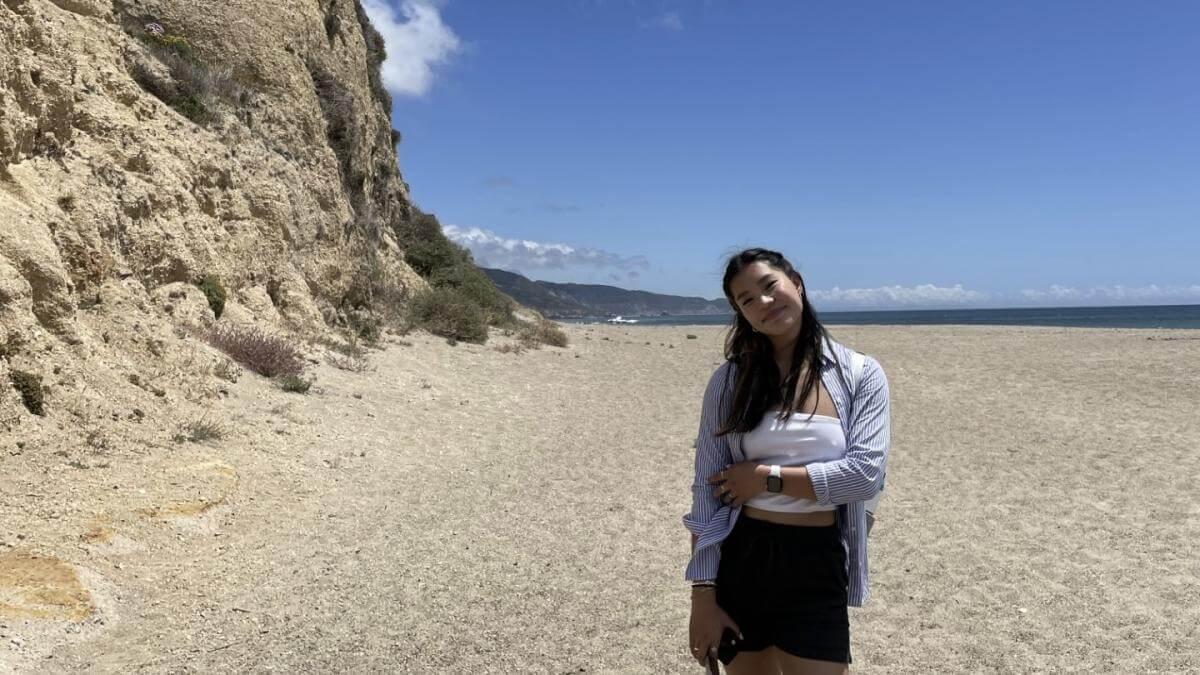Juliana standing on a sandy beach in the sunshine.