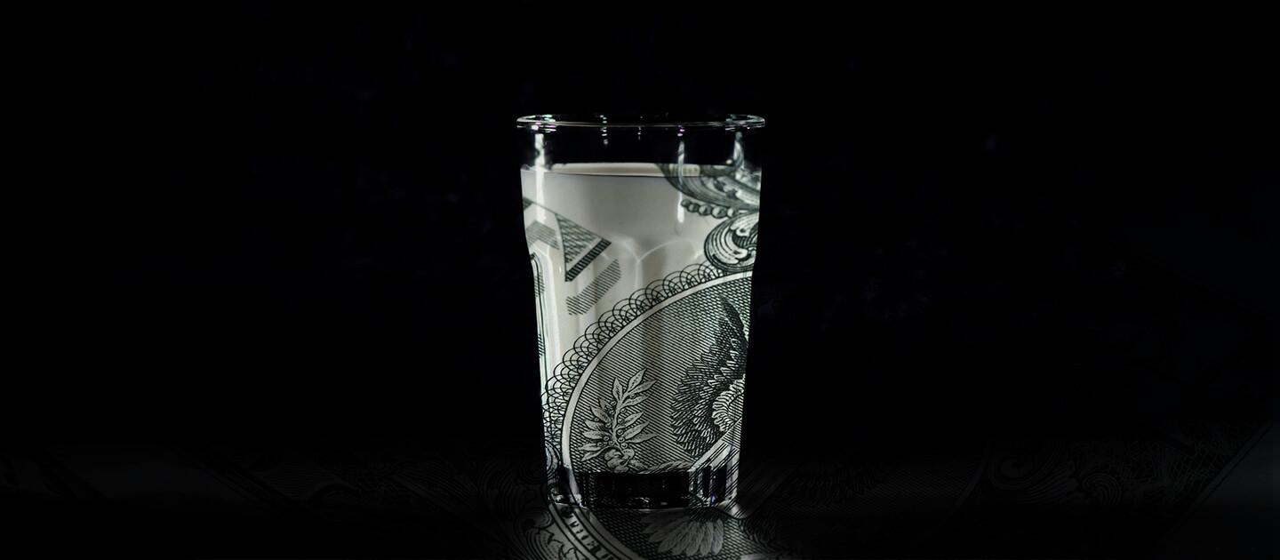 a glass of milk against a stark black background. the milk has been altered to show a dollar bill in it