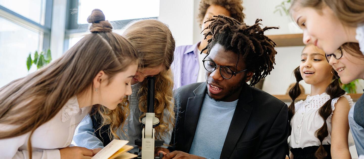 a teacher and six elementary school students gathered around a microscope