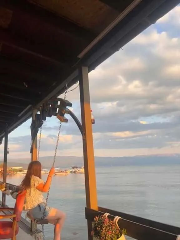 Woman sitting on a swing in front of water