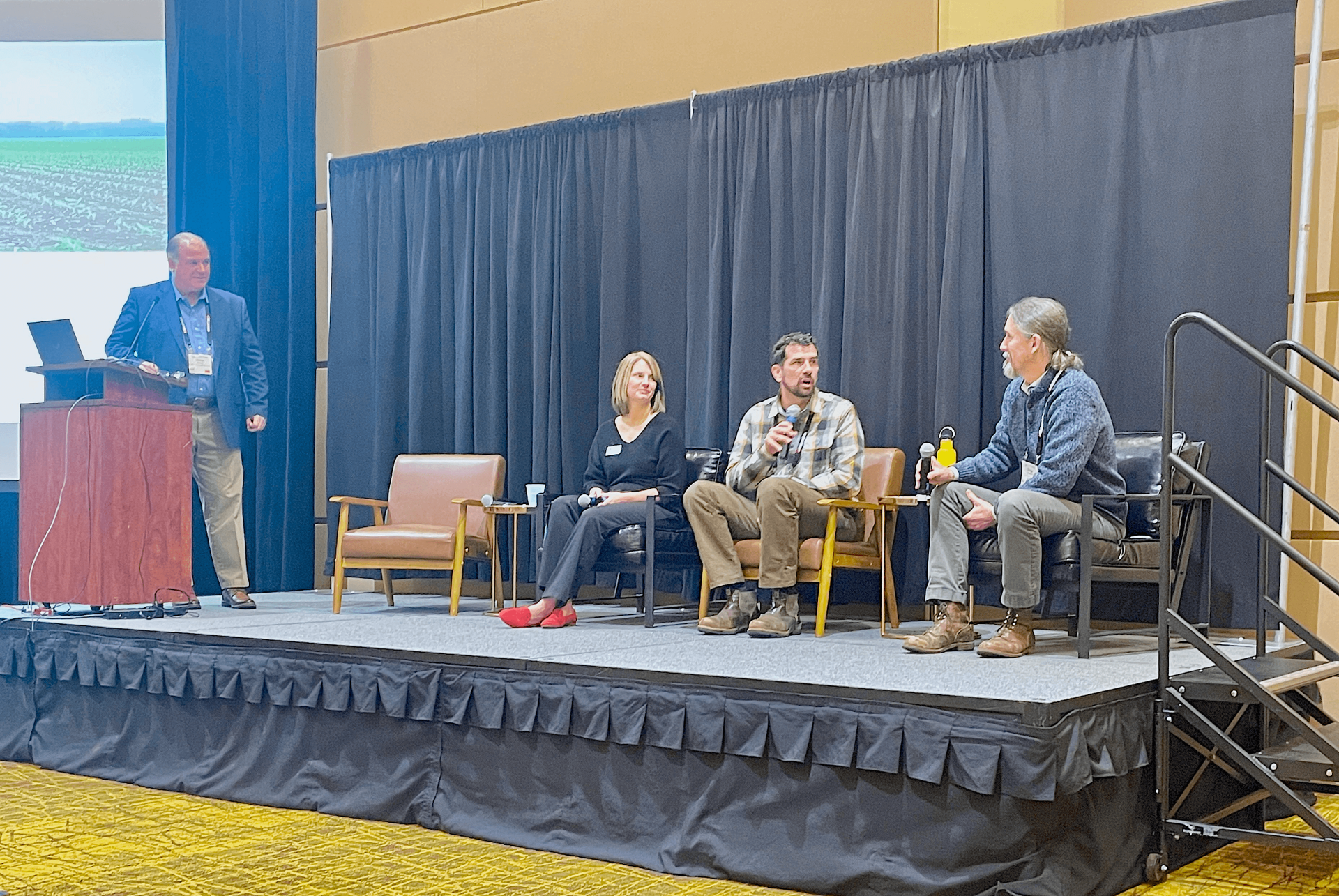 Three individuals on a stage and a moderator behind a lecturn