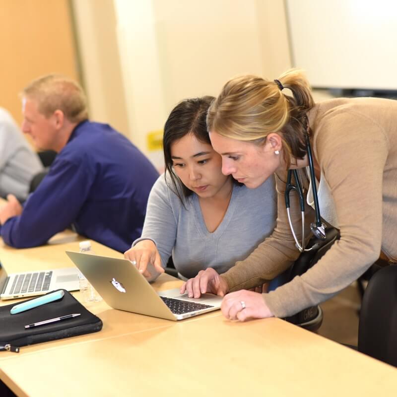 two people hunker over a laptop