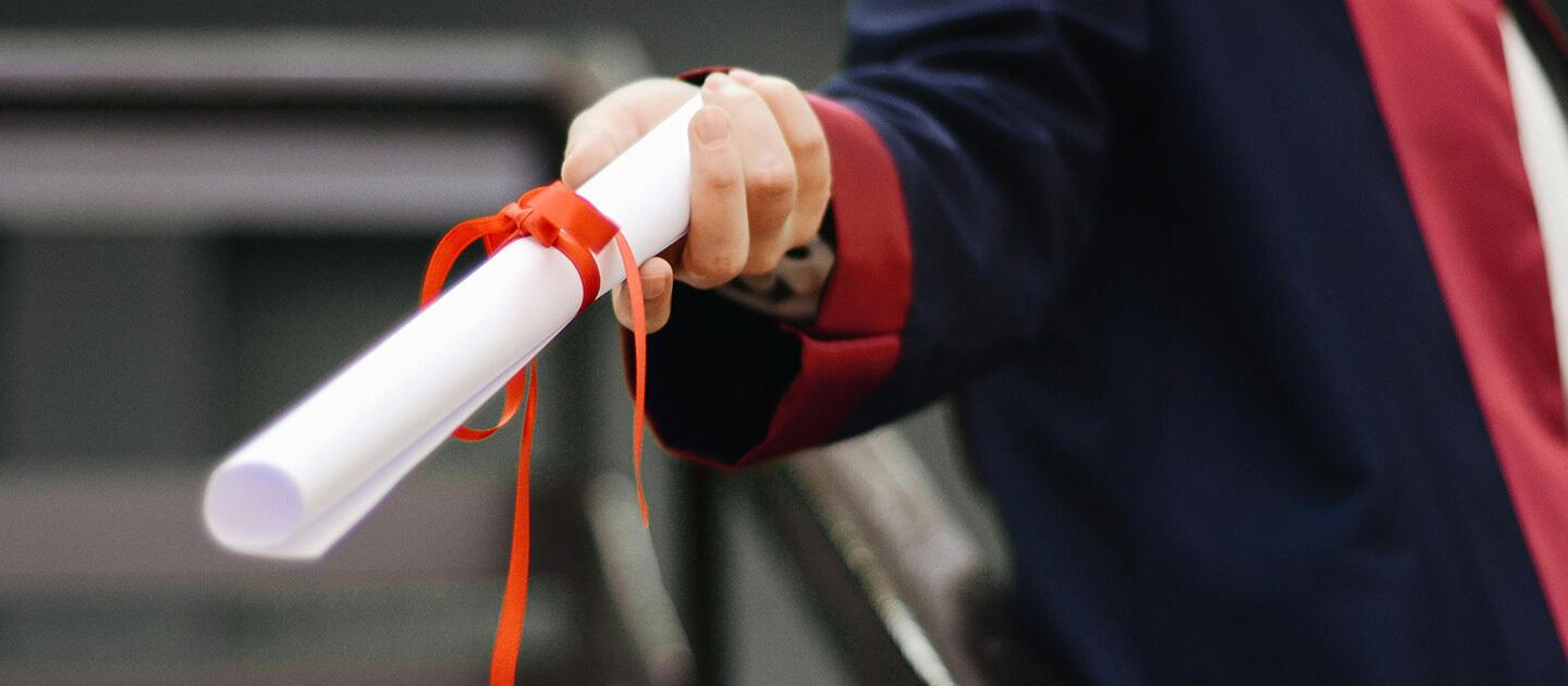 a hand reaching out holding a diploma wrapped in a ribbon