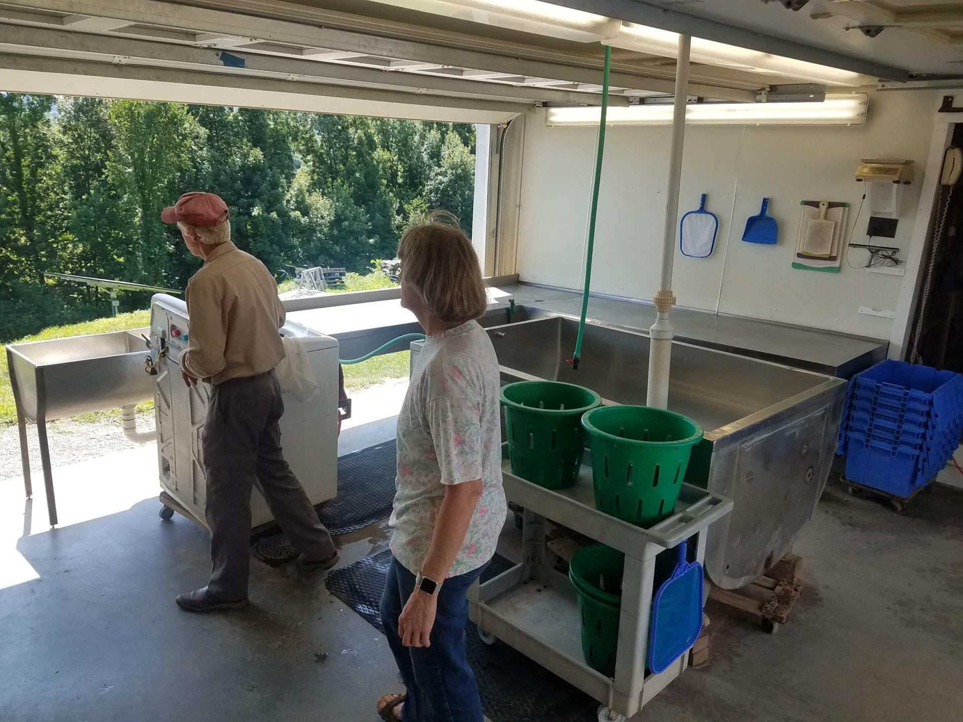 2 people next to a cart and a large sink