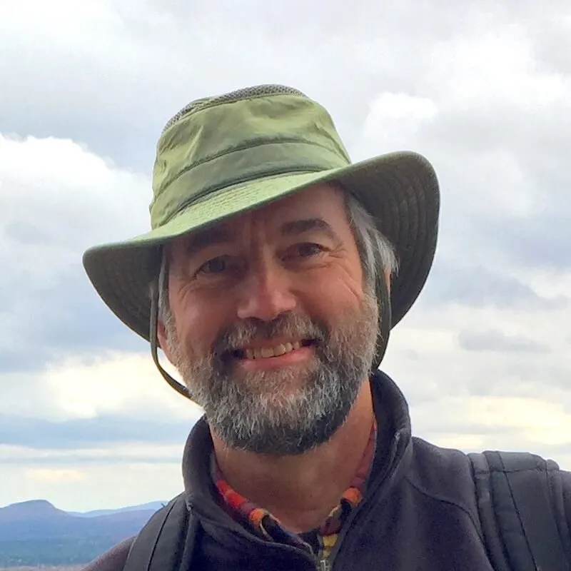 Walt in a green hat smiling against a cloudy sky
