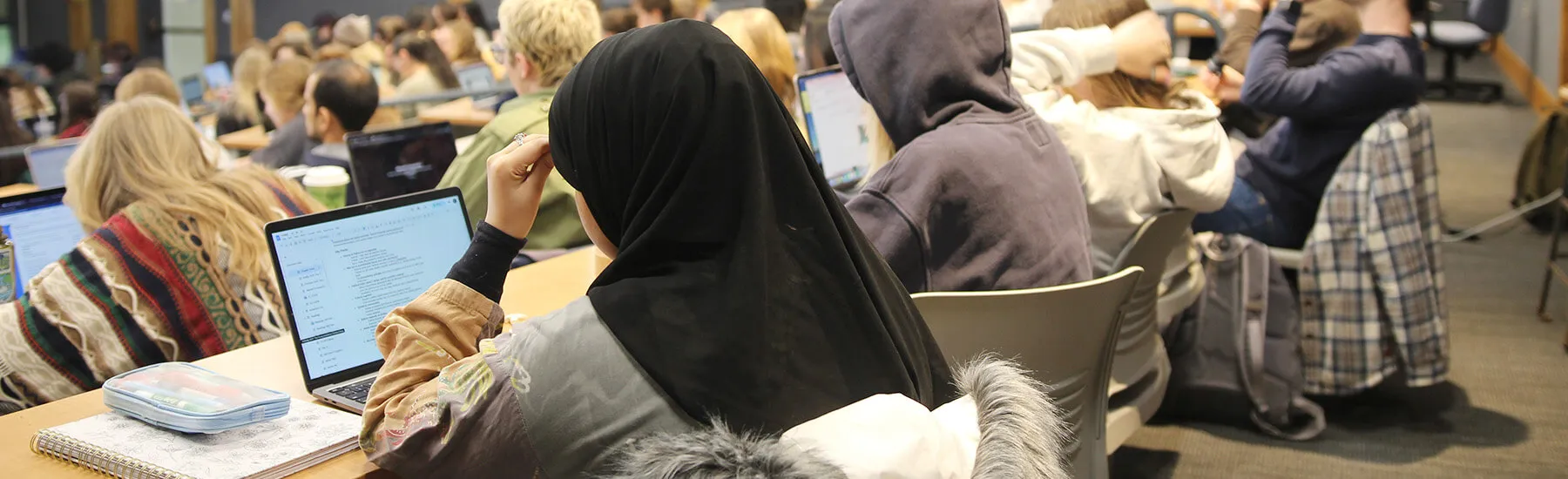  A crowd of students in a lecture hall, focused on the speaker at the front of the room.