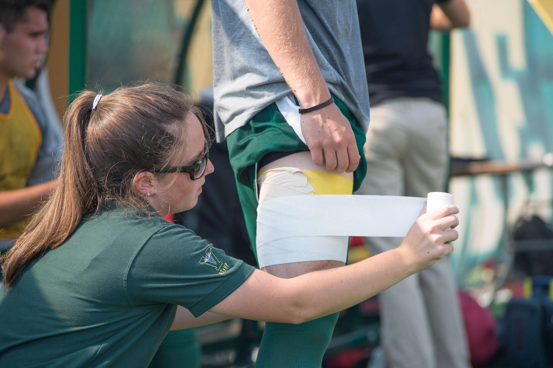 an athletic trainer applys tape to an athletes knee