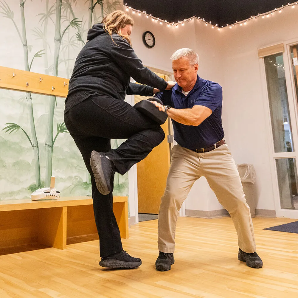 Women striking a pad with her knee that is being held by an instructor 