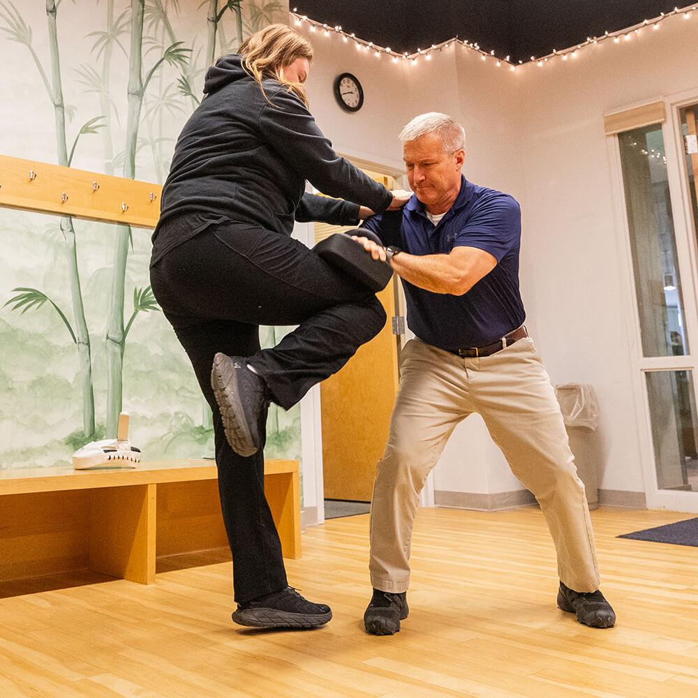 Women striking a pad with her knee that is being held by an instructor 
