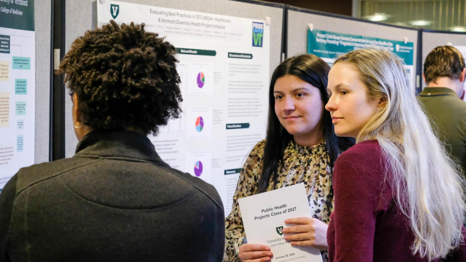 Three graduate students discuss a Public Health research poster
