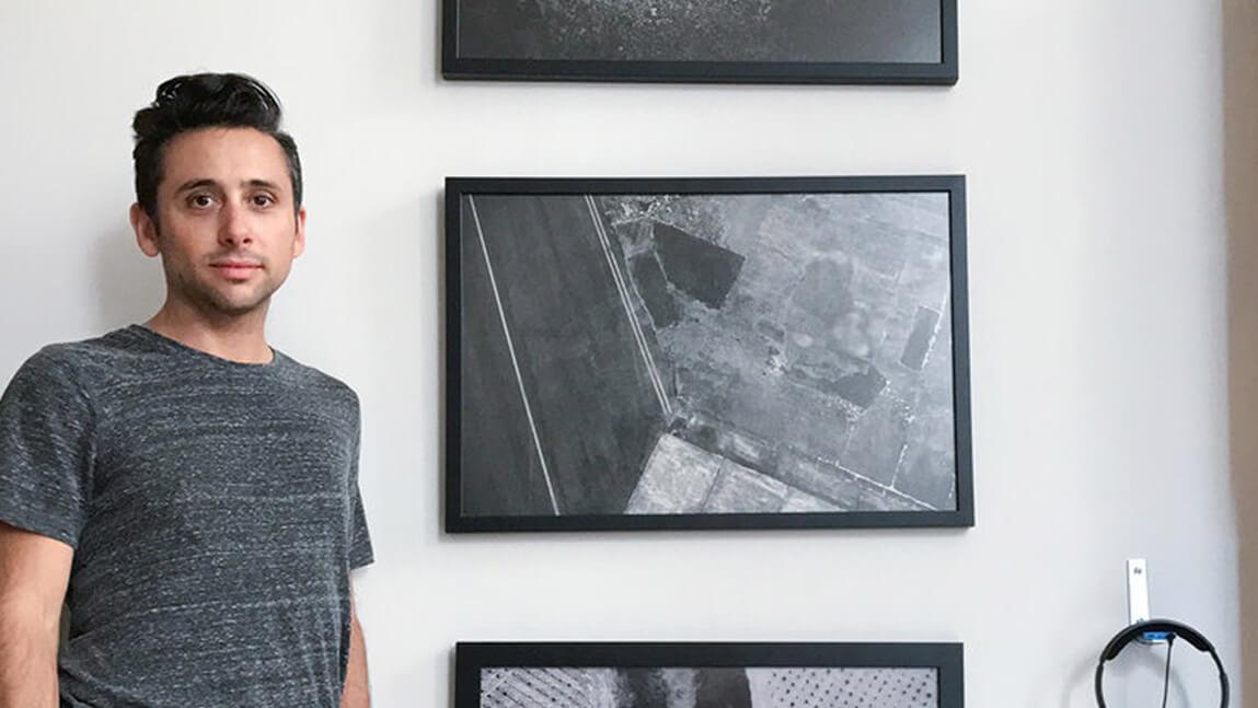 A man stands in front of a wall displaying three framed pictures