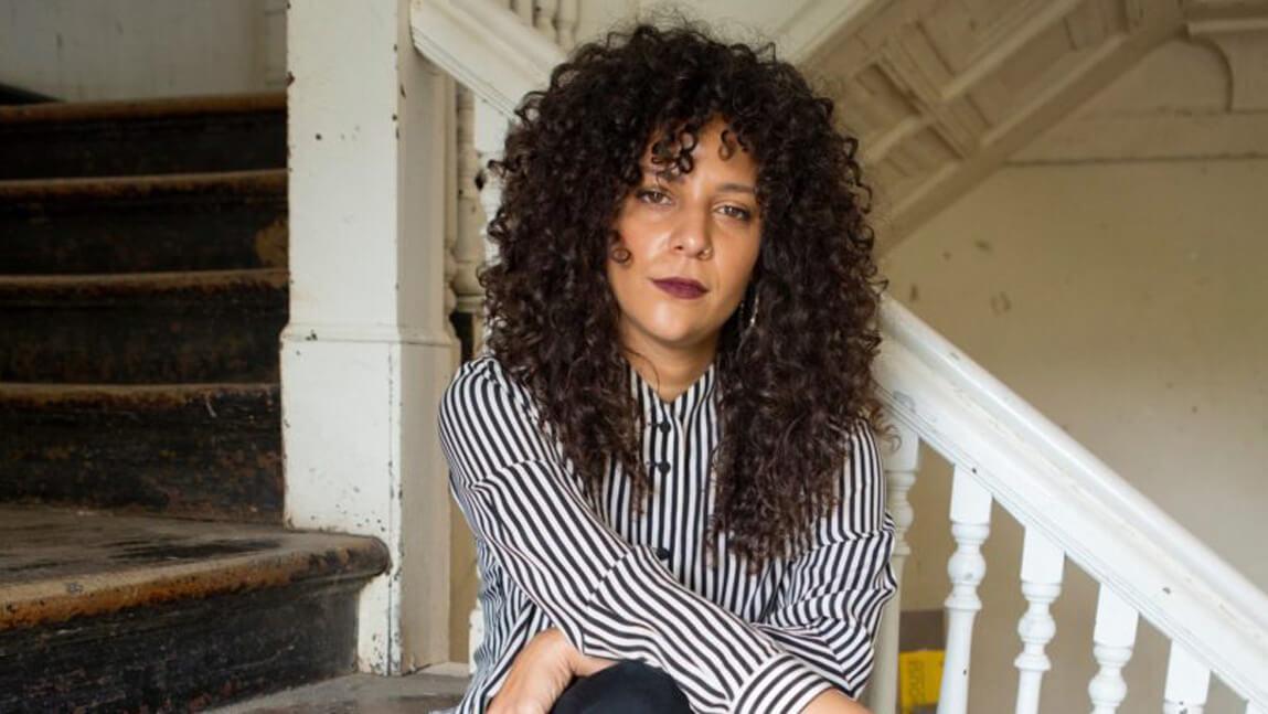 A woman with curly hair sits on a set of stairs