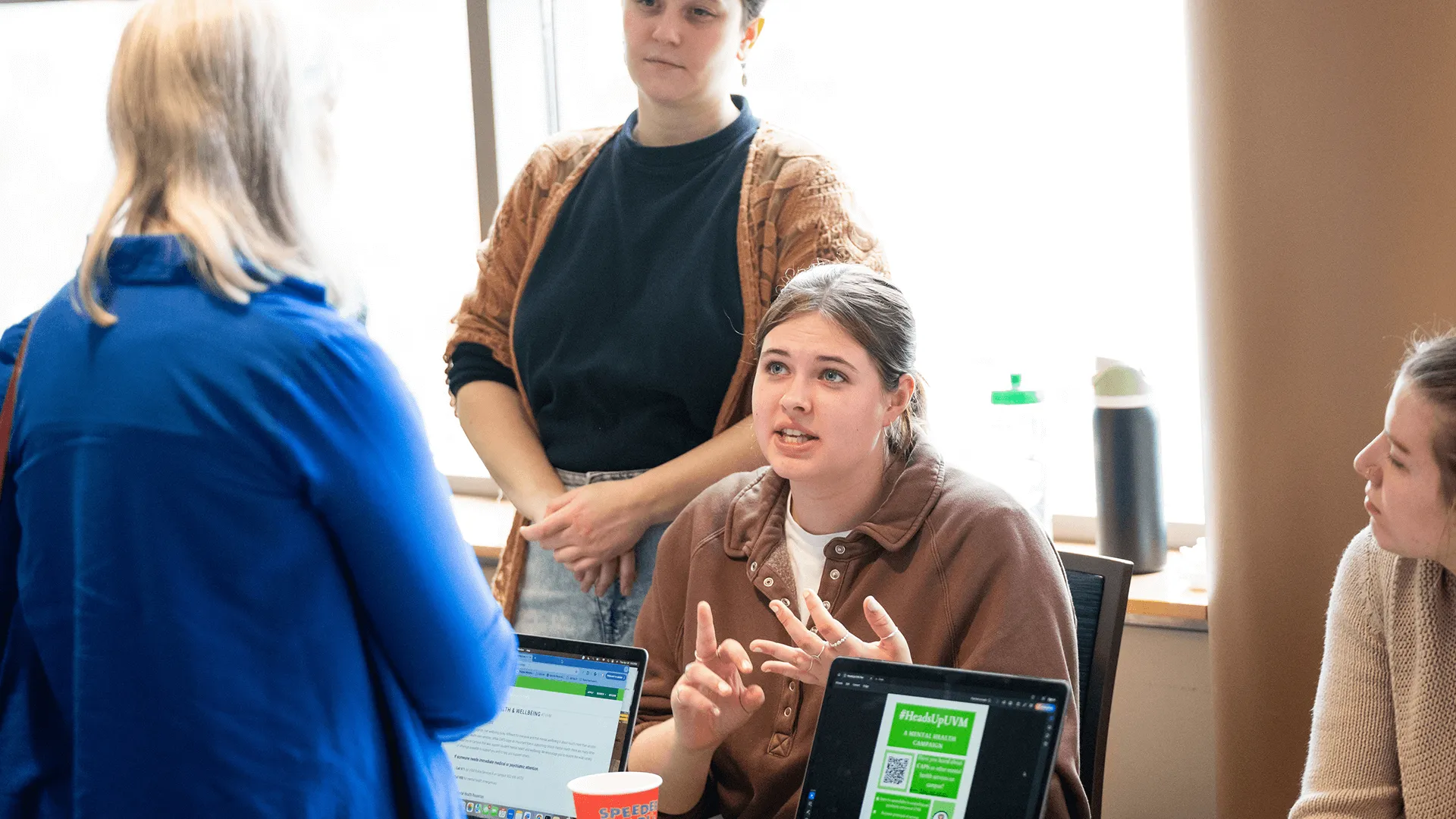 Student explains a slideshow presentation to an attendee during an indoor showcase event.