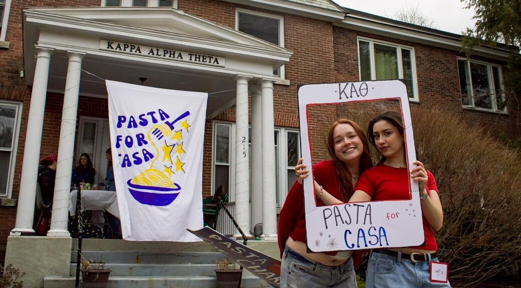 Two kappa alpha theta members pose outside of "Pasta for Casa" at their chapter facility 