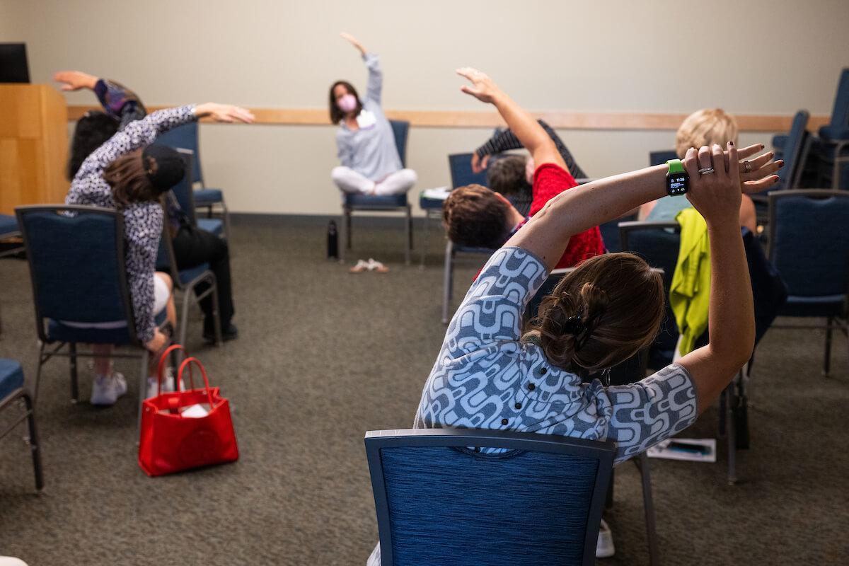 Several people sitting in chairs stretch, arms over their heads.