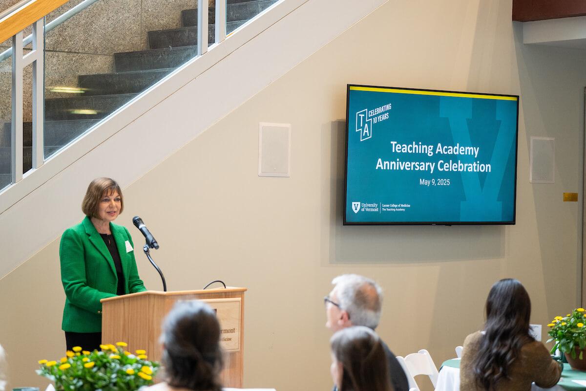 a woman at a podium in front of a computer screen and an audience
