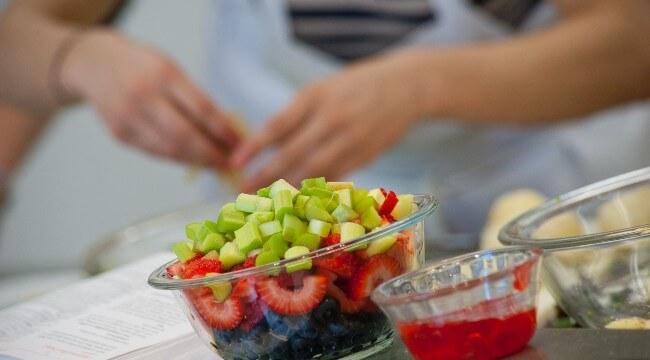 A bowl of chopped fruit with student cook in background