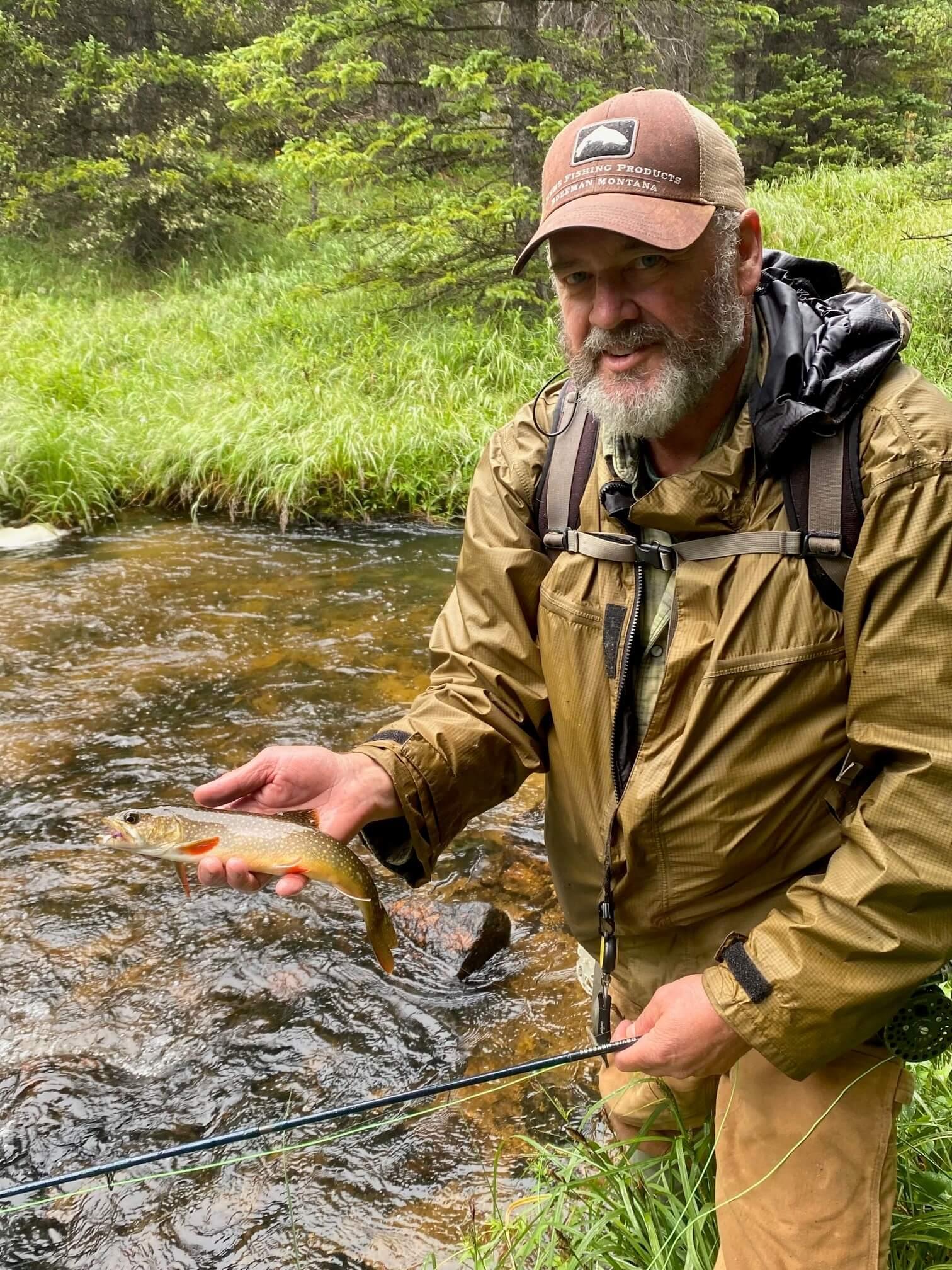 man by a stream holding a fish