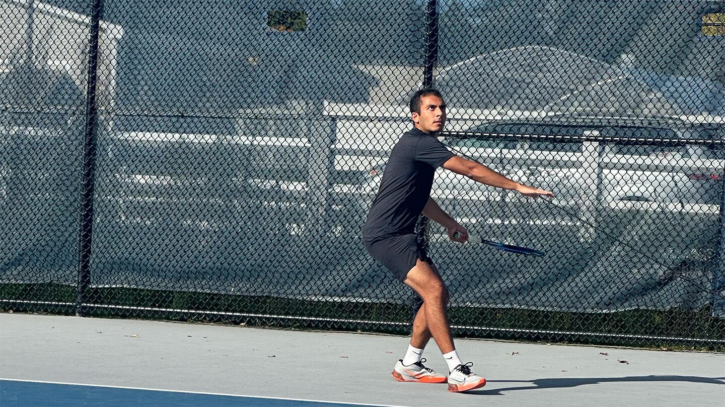 Young man with brown hair in gray t-shirt and shorts serving tennis ball on tennis court