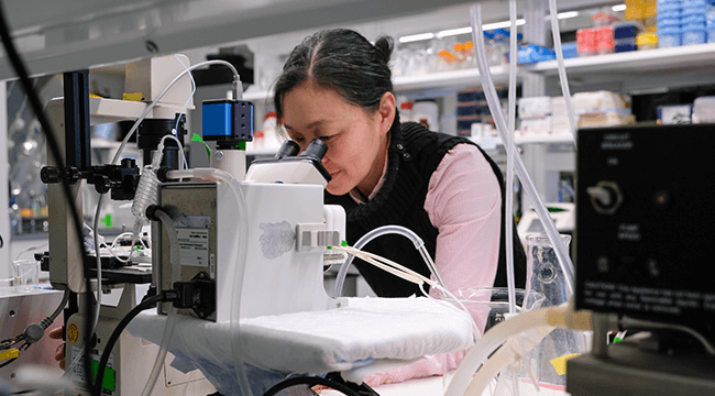 a woman looking into a microscope in a lab
