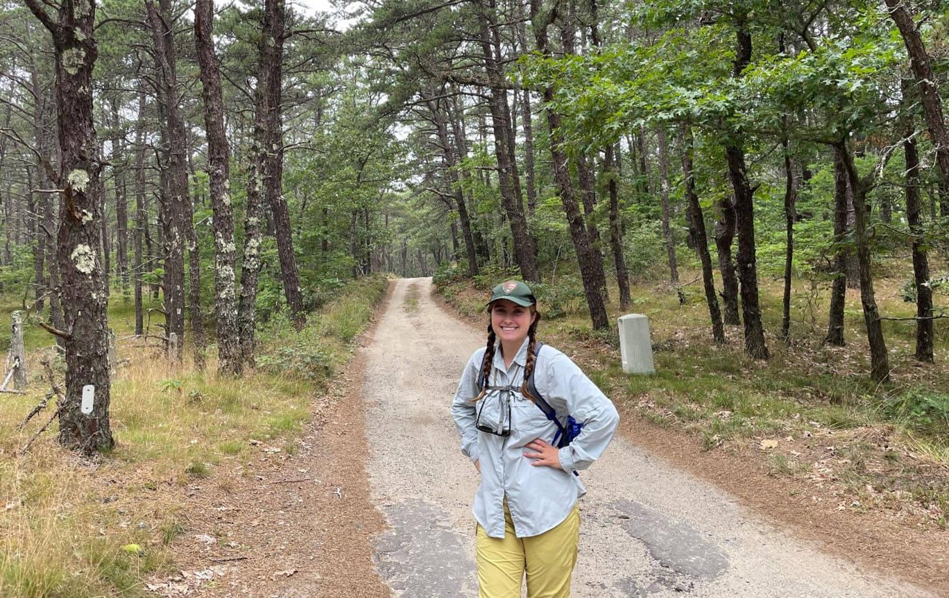 a woman stands on a dirt road in the woods