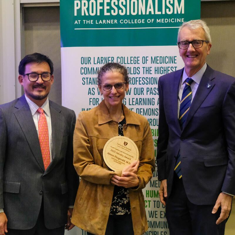 woman holding a plaque is flanked by two men in suits