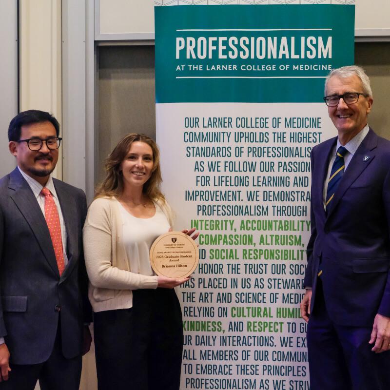 woman holding a plaque is flanked by two men in suits