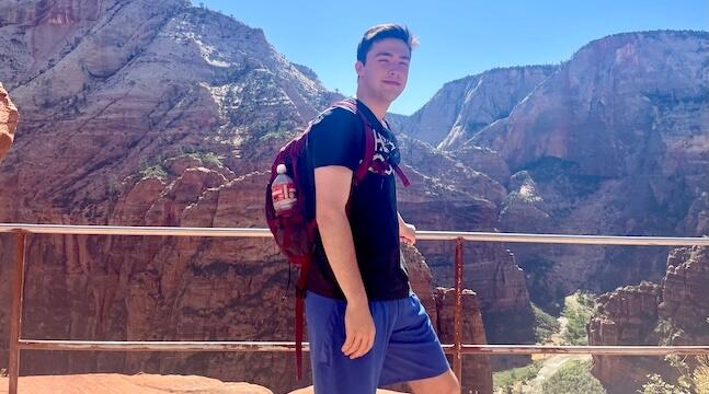 young man standing by railing next to a canyon
