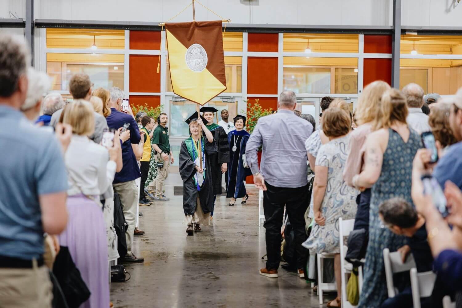 Rubenstein School commencement processional with the banner bearer and Interim President Patty Prelock in the background