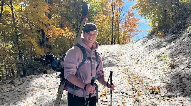 young man with skis on his back standing on snowy forest trail
