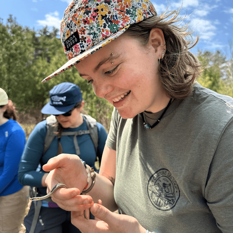 RSENR student in the field holding a small snake. The student has a colorful floral hat on.